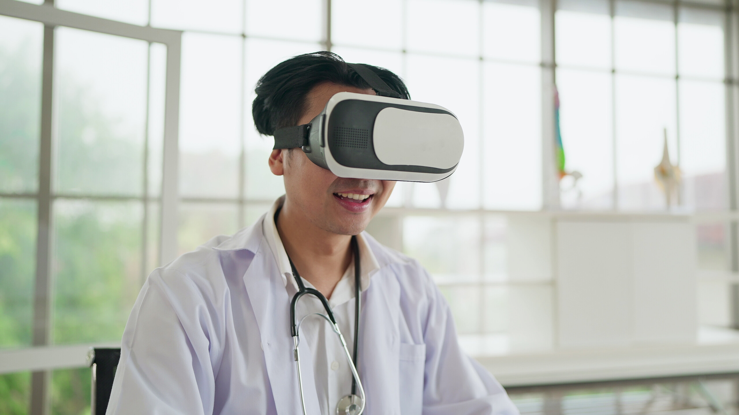 Happy young asian male doctor in uniform wearing VR headset and virtual interface. Future medicine and modern technologies gadgets in healthcare concept.