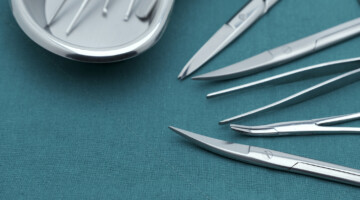 Basic surgical instrument scalpel forceps tweezers scissors in emesis or plus basin on surgical green drape fabric.