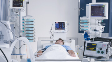 Patient in a hospital bed surrounded by equipment.