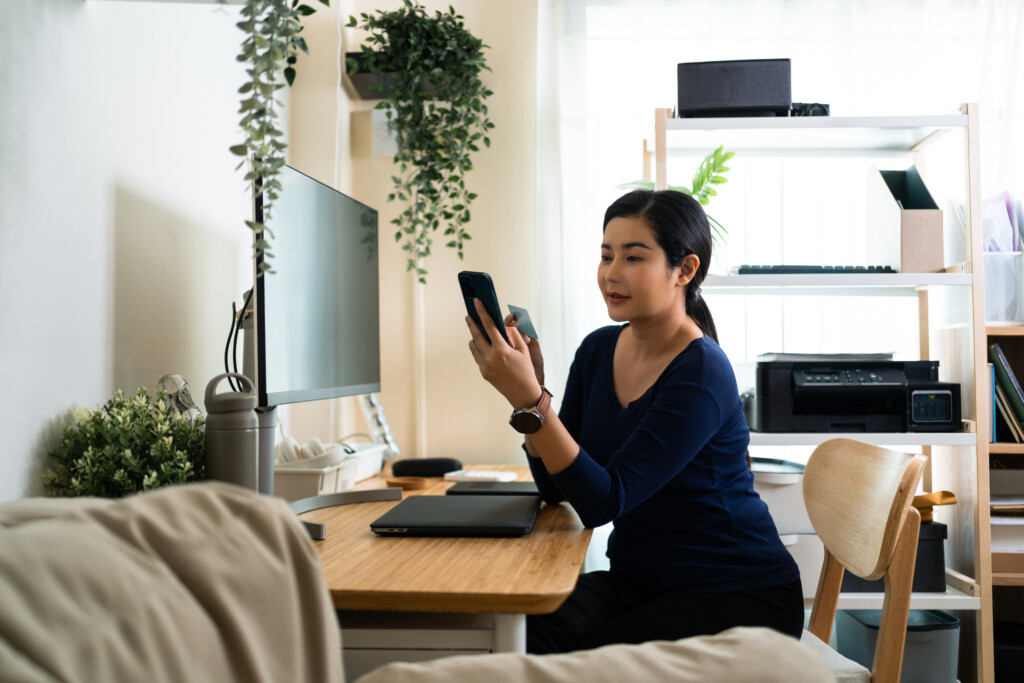 Comfortably seated at her workspace, a focused woman examines her health insurance ID card, ensuring her details are up-to-date amidst a home office setting.