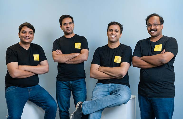 Four men and a blue background, all with arms crossed.