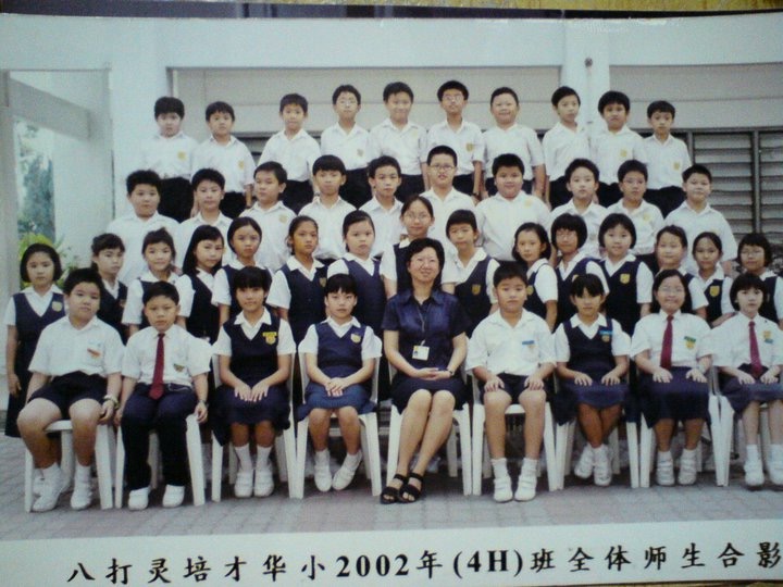 Large class photo of elementary school students in uniform posed with their teacher.