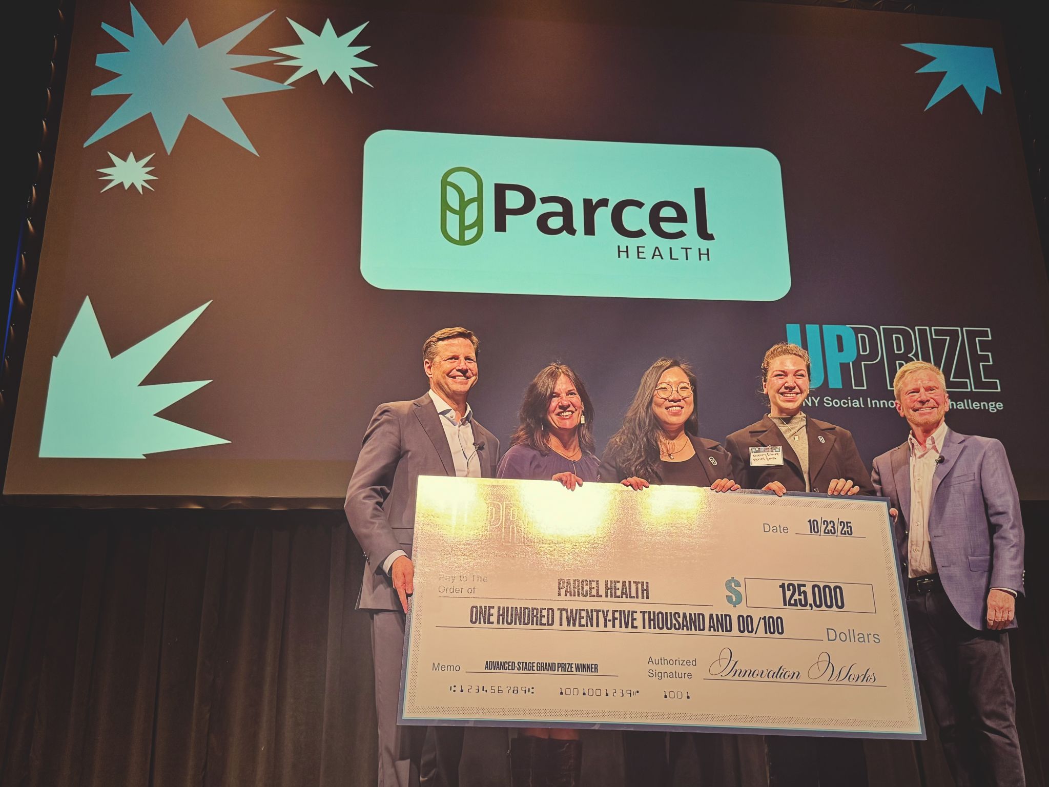 Group onstage holding an oversized check for $125,000 in front of a screen displaying the Parcel Health logo.
