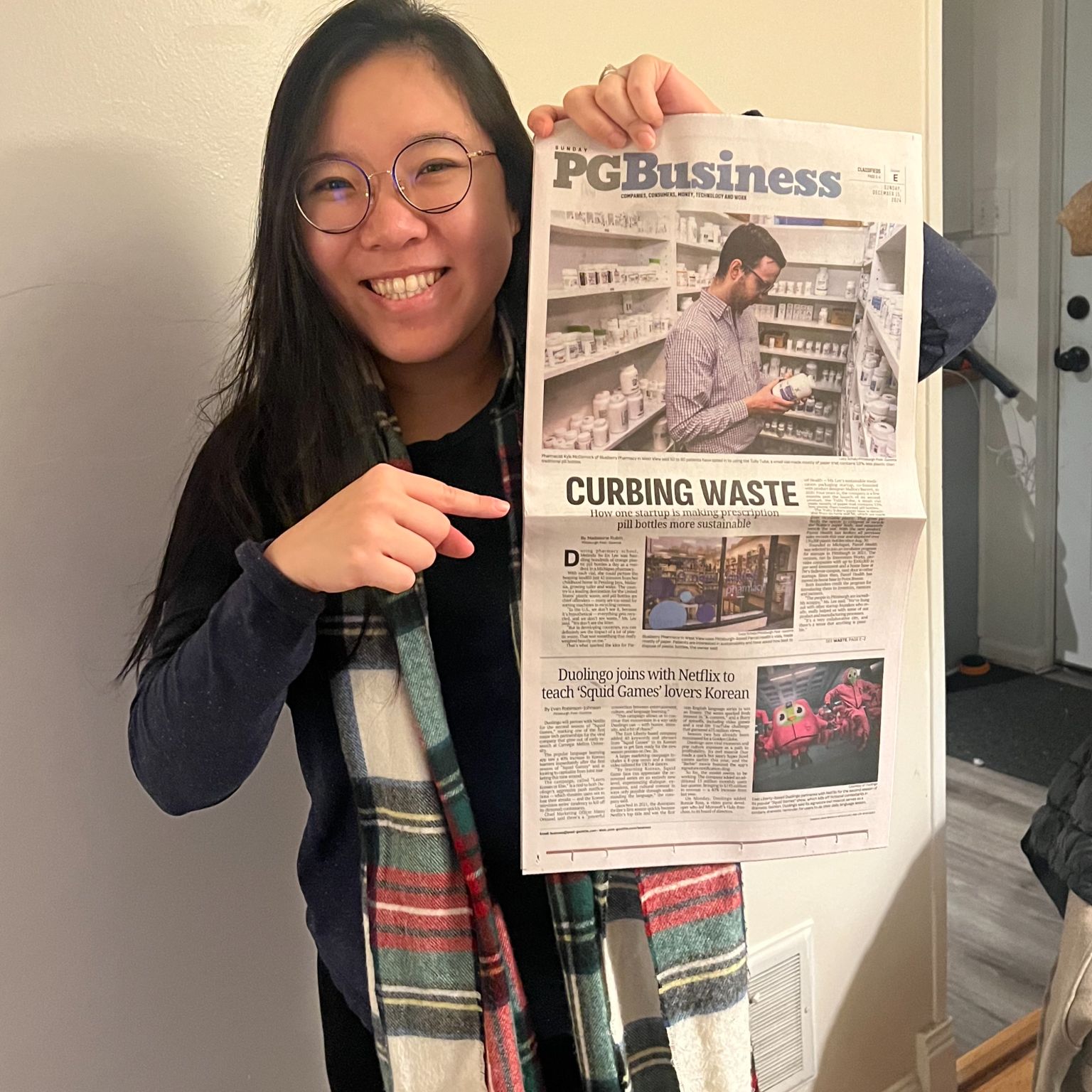 Woman smiling and holding up a newspaper featuring a front-page article titled “Curbing Waste.”