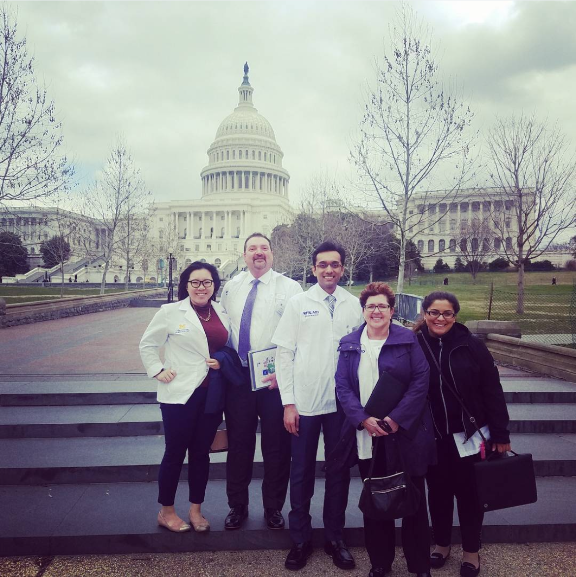 Group of five people standing in front of the U.S. Capitol building, some wearing white lab coats.